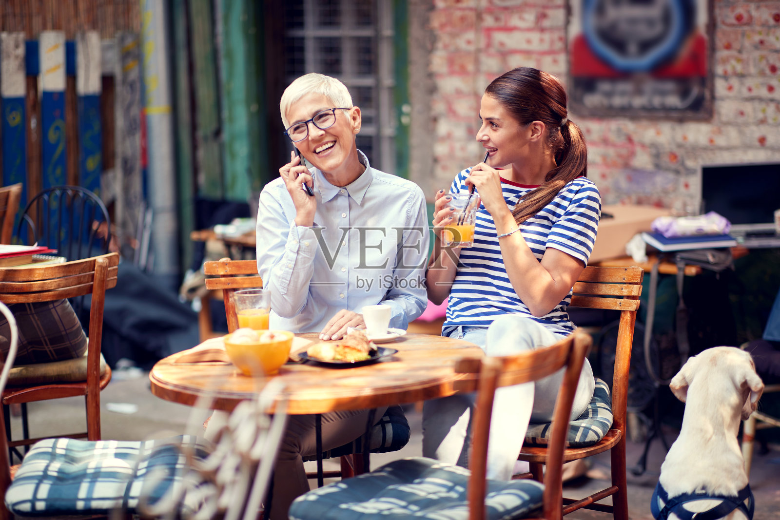 老妇人在打电话，面带微笑，而年轻的成年女性正在喝着果汁，带着迷人的微笑看着她照片摄影图片