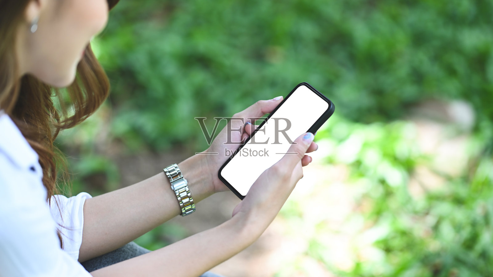 在公园里，一名年轻女子手持黑屏智能手机。照片摄影图片