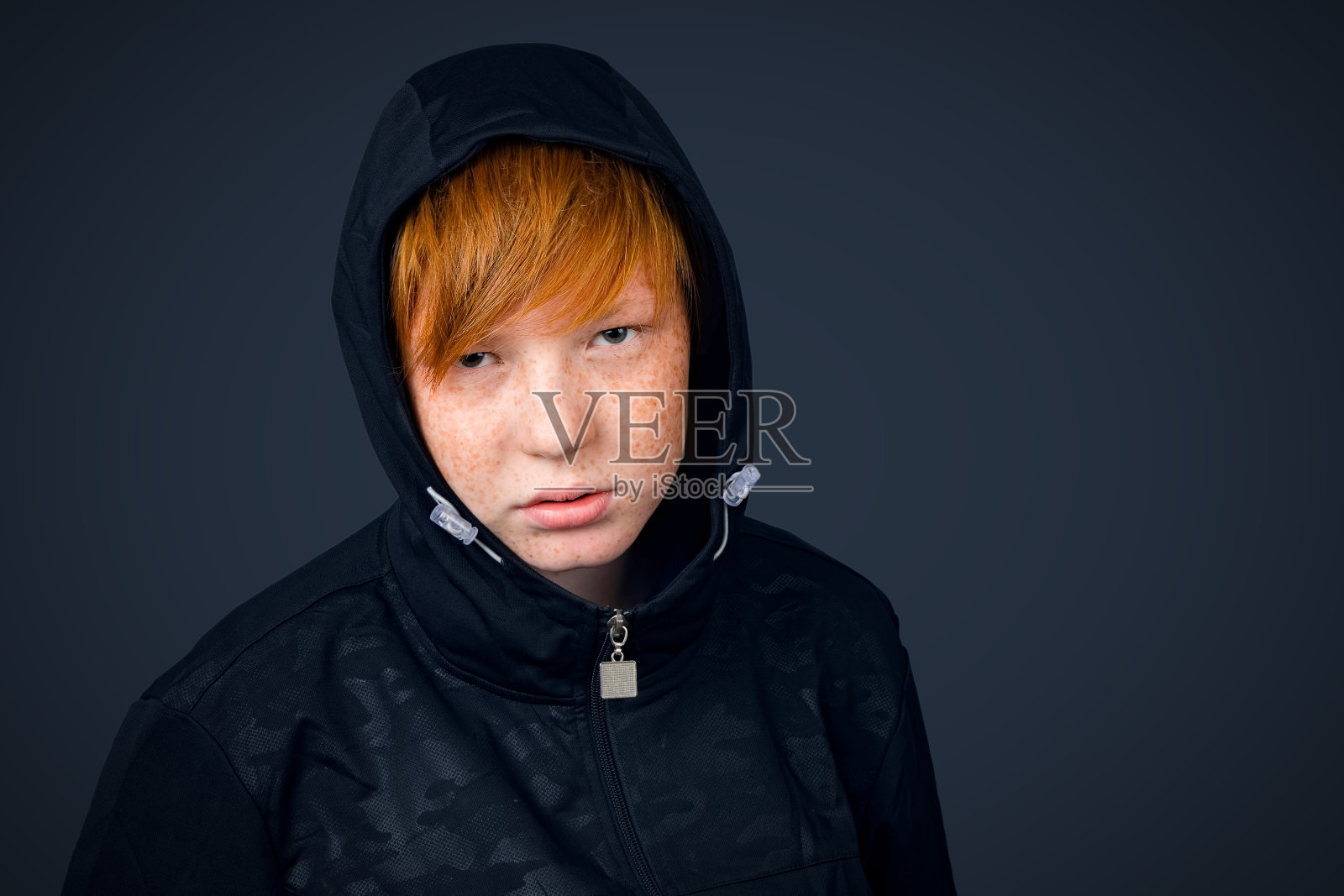 一名红发少年的肖像，身穿运动衫，戴着兜帽，背景为黑色。照片摄影图片
