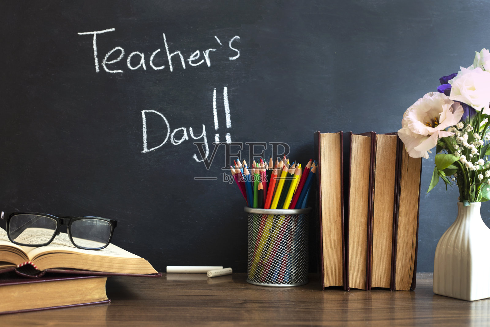 眼镜老师的书和一个站在桌子上的铅笔，在黑板的背景上用粉笔。教师节的概念。照片摄影图片
