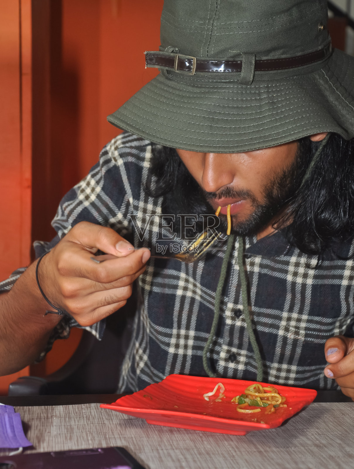一个留着胡子和长发的男人在咖啡馆吃面条，戴着乡下帽子的特写照片摄影图片