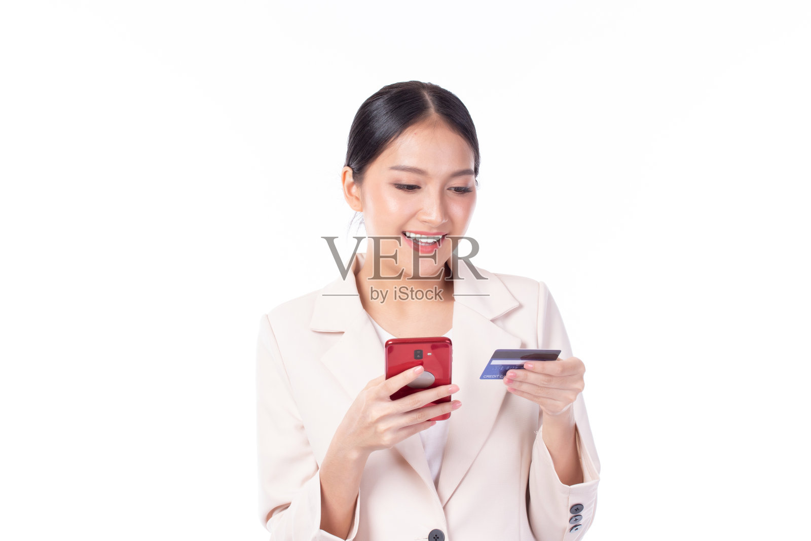 人像亚洲快乐的年轻女孩穿着粉红色的西装，快乐的微笑，拿出塑料信用卡，拿着手机，孤立在白色背景。商务网上购物的概念。照片摄影图片