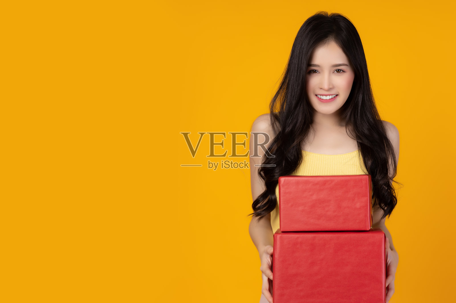 快乐的年轻女士收到红色的礼品盒或新年礼品盒或圣诞礼物盒与微笑的脸和幸福站在黄色的背景复制空间圣诞节生日和新年的概念照片摄影图片
