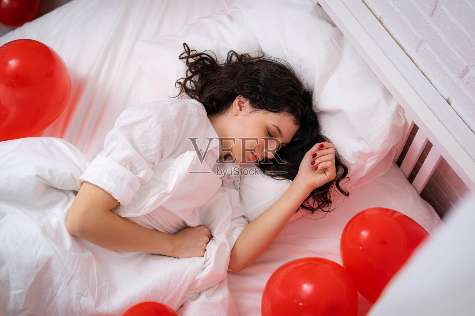 深色皮肤的欧洲女孩睡在床上红色的心形气球。情人节早上的惊喜礼物照片摄影图片
