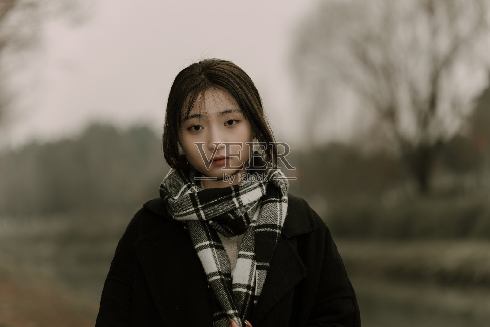 一个孤独的亚洲女孩戴着围巾在一个阴天的湖边照片摄影图片