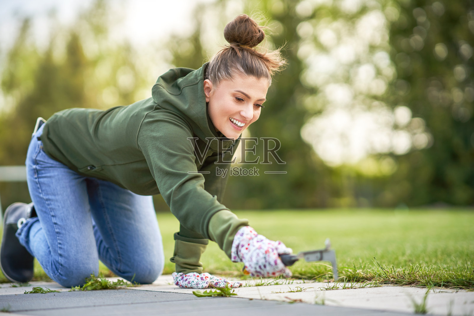 一个年轻的女人在花园的混凝土中拔除杂草照片摄影图片