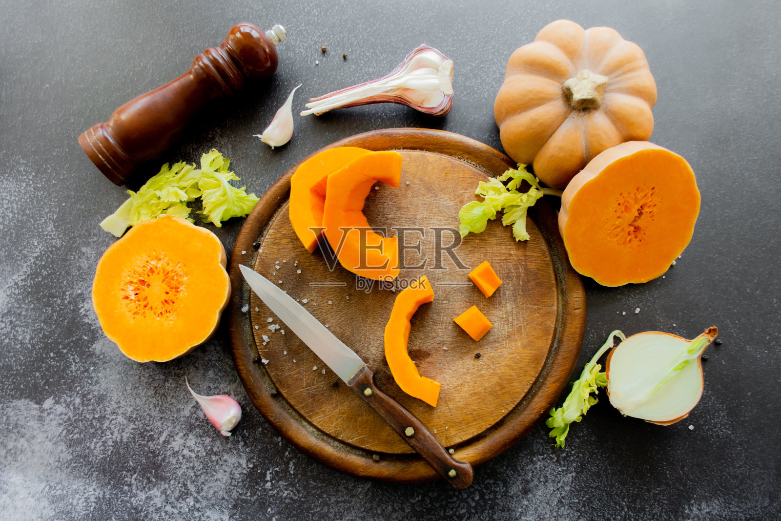 新鲜鲜亮的南瓜用刀放在木板上。芹菜和大蒜，洋葱和散花椒和盐与香料磨照片摄影图片