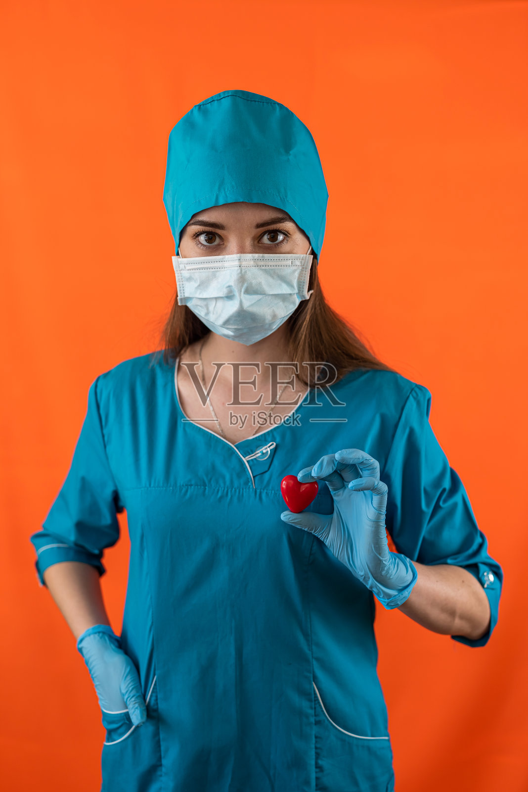 医院手术室里，护士穿着蓝色工作服，戴着口罩手套，捧着小红心。照片摄影图片