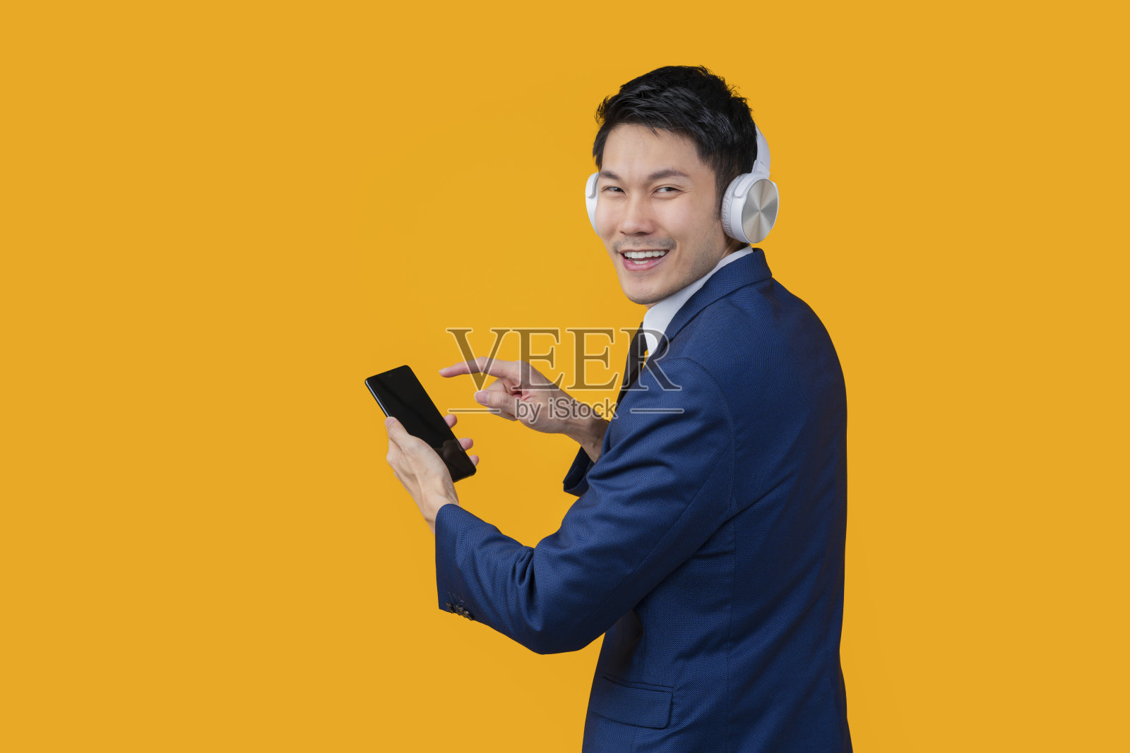 聪明休闲的亚洲男性商务正装，戴耳机，手从智能手机移动应用程序选择播放列表歌曲，下班后放松休闲，在黄色背景下隔离工作室拍摄照片摄影图片